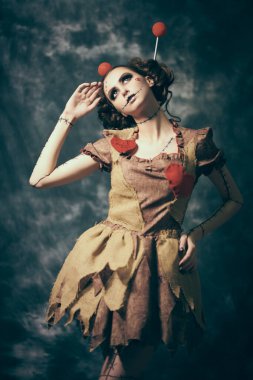 Cadılar Bayramı kutlaması. Makyajlı, saç stili ve voodoo bebeği elbisesi olan güzel bir kız klasik bir arka planda kurnazca poz veriyor. Voodoo kültürü.