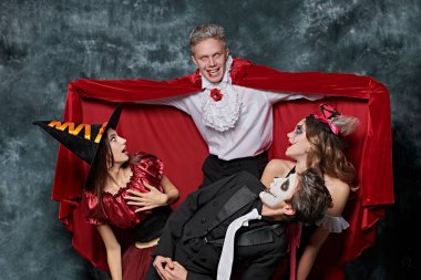 Teenage friends in carnival costumes have fun celebrating Halloween. Skeleton, witch, clown and vampire. Merry Halloween party. Studio portrait on vintage background. clipart