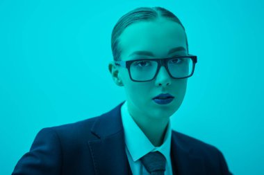 Resmi takım elbiseli, turkuaz ışıklı kravat ve gözlüklü zarif bir genç bayanın portresi. İş modası. Gözlük stili. Stüdyo çekimi.