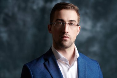 İş konsepti. Gözlüklü ve takım elbiseli yakışıklı bir işadamının portresi, kameraya ciddi ve emin bir şekilde bakıyor. Stüdyo resmi.