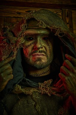 Yüzünde yara izleri olan korkunç sakallı bir adam, çuval bezinden giysiler giymiş, korkunç siyah gözlerle ahşap bir eve bakıyor. Korku fantezi romanı. Cadılar Bayramı. Frankenstein canavarı.