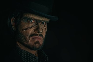 Yüzünde ve boynunda kocaman yaralar olan, zarif siyah bir takım elbise ve siyah bir fonda silindir şapka giymiş korkutucu gizemli bir adamın portresi. Gotik korku romanı. Cadılar Bayramı. Boşluğu kopyala.