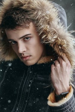 Dışarıda karlı bir günde kışlık ceketli, kürklü, yakışıklı bir erkek model. Erkekler kış modası. 