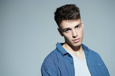 Gençler. Kameraya sakince bakan sıradan giyinmiş yakışıklı bir esmer adamın stüdyo portresi. Erkek güzeli. Gri arka plan. Boşluğu kopyala.