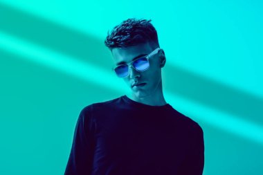 Siyah günlük kıyafetler ve parlak mavi bir arka planda poz veren gözlüklü bir adam. Erkek modası ve tarzı. Boşluğu kopyala.