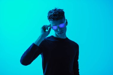 Siyah günlük kıyafetler ve parlak yeşil arka planda poz veren moda güneş gözlüklü yakışıklı genç bir adamın portresi. Erkek modası ve tarzı.