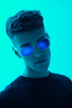 Parlak yeşil arka planda siyah günlük kıyafetler ve güneş gözlüğü takan modaya uygun yakışıklı bir adam. Erkek modası ve tarzı.