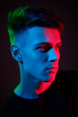 Yakışıklı, genç ve esmer bir adamın sakince yana baktığı yakın çekim. Kırmızı ve yeşil ışıkta siyah arkaplan. Gençler. Erkek güzeli.. 