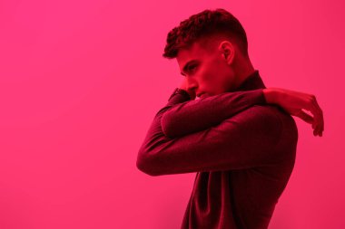 Parlak pembe bir arka planda balıkçı yaka giyen çekici bir esmer adamın profil portresi. Erkek modası ve tarzı. Boşluğu kopyala.