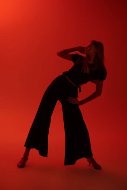 Siyah bluzlu, geniş pantolonlu ve ayakkabılı çekici bir kız stüdyoda kırmızı ışıkta dans ediyor. Güzellik ve Moda. Modern bale dansları. 