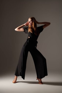 Stüdyoda siyah bluz, pantolon ve ayakkabılarla dans eden zarif güzel bir kızın portresi. Güzellik ve Moda. Modern bale dansları.