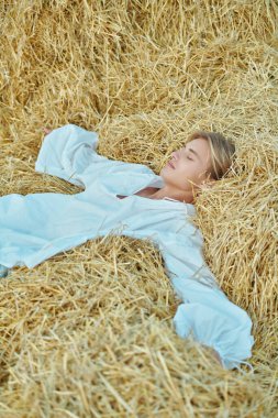 Beyaz, klasik gömlekli, geniş kollu çekici sarışın bir adam sonbahar tarlasında samanların üzerinde gözleri kapalı yatıyor. Romantik tarzda. Bir aşk hikayesinin kahramanı..