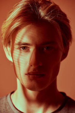 Erkek güzeli. Turuncu stüdyo arka planında yüzü gölgeli yakışıklı bir sarışının resim çekimi.. 