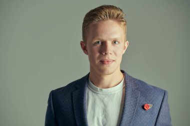 Beyaz tişörtlü, ceketli, gri arka planda güvenle gülümseyen zarif, modern bir gencin portresi. Gençler, başarı..