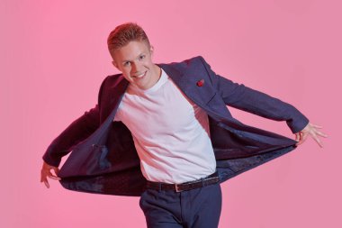 Zarif takım elbiseli, pembe arka planda duygusal poz veren gülümseyen genç bir adamın portresi. Başarılı gençler..