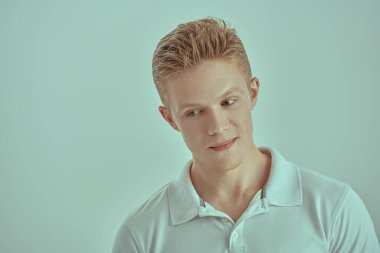 Beyaz polo tişörtlü yakışıklı sarışın bir adam gülümsüyor ve düşünceli bir şekilde uzaklaşıyor. İnsanlar ve duygular. Beyaz arkaplan. 