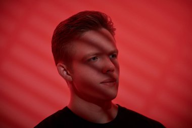 Yüzünde gölgeler olan genç ve yakışıklı bir adamın düşünceli bir şekilde yan tarafa baktığı bir fotoğraf. Kırmızı arka plan. Gençler. Erkek güzeli..