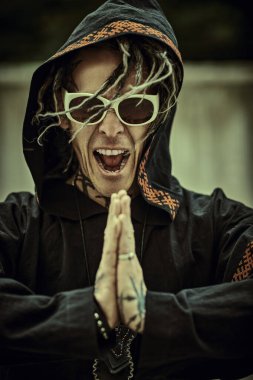 Rock ve punk kültürü. Rastalı ve siyah etnik elbiseli olağanüstü olgun bir adam sokakta elleri sımsıkı bağlı ve bağırıyor.. 