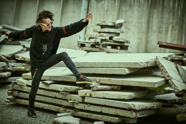 Rasta saçlı, siyah elbiseli, etnik süslemeli dövmeli olağanüstü olgun bir adam arka sokakta açıkça poz veriyor. Rock ve punk kültürü. Boşluğu kopyala.