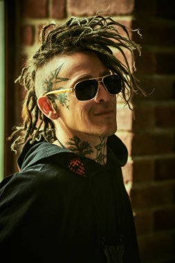 Serseri alt kültürü. Rock tarzı. Etnik dövmeleri ve punk stili Mohawk rastaları olan olgun, vahşi bir adam bir çatı katında duruyor.. 