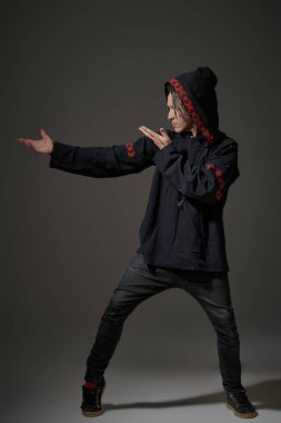 Siyahi etnik kıyafetleri ve dövmeleri olan modern bir erkek şamanın büyülü bir ayin yaptığı uzun bir çekim. Şamanik uygulamalar. Gri stüdyo geçmişi.