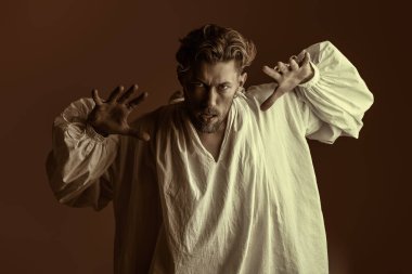 Beyaz, klasik tişörtlü, geniş kollu, kızgın bir şekilde kameraya bakan kızıl saçlı bir adamın portresi. Kahverengi arka plan. Tarihi portre, 19. yüzyıl sonu - 20. yüzyıl başı. Tiyatro.