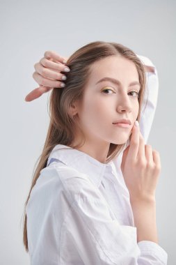 Beyaz bir arka planda beyaz gömlekle poz veren kahverengi saçlı güzel bir kız. Moda ve güzellik. Kadın Sağlığı.
