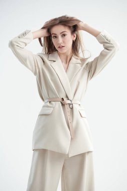 Kadın modası işte. Beyaz bir arka planda zarif bej bir takım elbiseyle poz veren güzel bir manken. Zarif bir tarz. Stüdyo çekimi. 