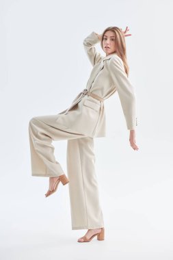 Zarif bir tarz. Güzel bir manken beyaz arka planda bol bej bir takım elbiseyle poz verir. Kadın modası. Tam boy stüdyo resmi..