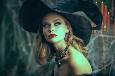 Şapkalı, omuzları açık, zarif makyajlı ve eski kalesinde örümcek ağıyla kaplı takıları olan büyüleyici genç bir cadı. Cadılar Bayramı için peri masalları. Cadılar Bayramı Cadısı. 