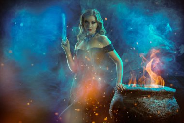 Cadılar Bayramı büyüsü. Omzundan çıkan zarif siyah elbisesi olan genç ve güzel bir cadı sihirli bir değnekle bir kazanın üzerinde gece ortaya çıkıyor. Boşluğu kopyala.