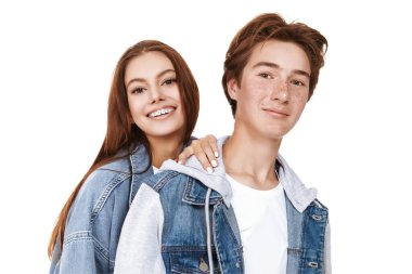Beyaz bir arka planda poz veren, son moda kot elbiseli, gülümseyen genç bir erkek ve genç kız portresi. Denim tarzı, gençlik tarzı..