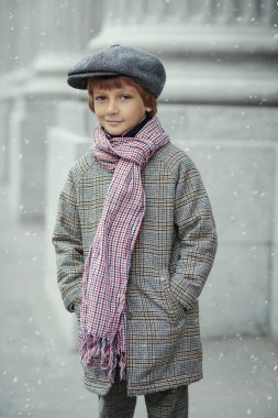 Çocuk modası. Retro tarzı. Sokakta elleri cebinde duran, retro tarzı ceketli, şapkalı ve eşarplı küçük bir çocuğun portresi. Karlı gün, kış mevsimi.
