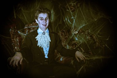 Vampirler. Yakışıklı bir genç vampir aristokrat eski kalesinde eski bir koltukta oturur ve şeytanca sırıtır. Vampirler hakkında bir roman. Cadılar Bayramı. Boşluğu kopyala. 