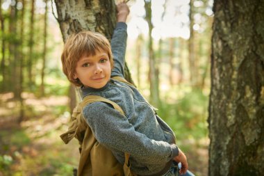 Eko-turizm. Sırt çantalı mutlu bir çocuk ağaçların arasında bir yaz ormanında duruyor ve gülümsüyor. Macera ve seyahat tutkusu.