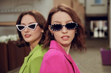 Şık güneş gözlüklü çekici esmer kızlar şehrin caddesinde yan yana duruyorlar. Yaz tarzı ve moda. Yaz tatili. 