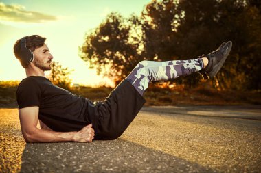 Spor kıyafetleri içinde sportif bir adam parkta fiziksel egzersiz yapıyor ve kulaklıklarıyla müzik dinliyor. Spor ve aktif yaşam tarzı. 