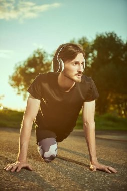 Kafasında kulaklık olan atletik bir adam gün batımında dışarıda egzersiz yapıyor. Aktif ve sağlıklı bir yaşam tarzı. Spor hobileri.