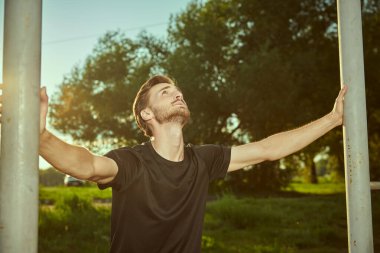 Aktif bir genç adam gün batımında parktaki yatay bir barda barfiks çekecek. Spor açık havada. Aktif ve sağlıklı yaşam tarzı.