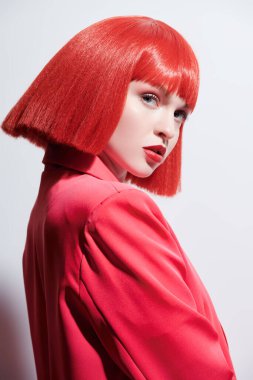 Moda ve kırmızı renk. Kırmızı peruklu ve kırmızı ceketli güzel bir mankenin portresi. Güzellik, saç stili ve makyaj.