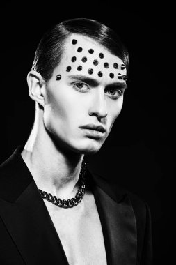 Çekici genç bir adam siyah arka planda metal dikenli siyah bir palto giyiyor. Moda fotoğrafı. Siyah beyaz portre.