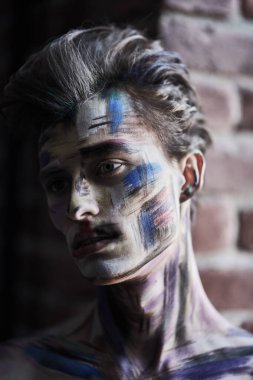 Vücut boyama, sanat. Duvarın arka planında dalgın dalgın duran boyalarla kaplı yakışıklı genç bir adamın portresi. Sanat ve erkek güzelliği.
