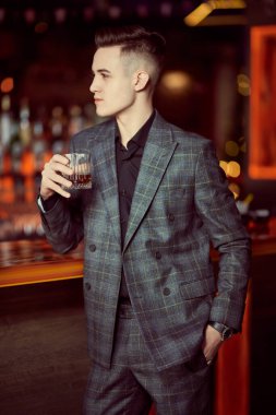 Pahalı takım elbiseli yakışıklı bir gencin portresi. Bir restoranda bir bardak viskiyle rahatlıyor. Lüks bir yaşam tarzı. İş adamı. 