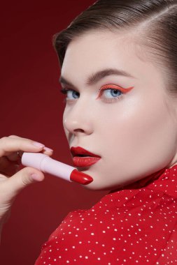 Sevimli kırmızı renk. Güzel, sarışın bir mankenin parlak kırmızı bir ruj tutarken yakın plan fotoğrafı. Makyaj ve kozmetik. 