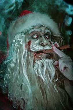 Noel ve Cadılar Bayramı. Korkunç yaşlı, zombi Noel Baba puro içiyor ve karanlık bir Noel odasında dikilirken ellerini kızgın bir şekilde ovuyor..