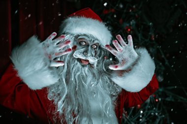 Korkunç zombi Noel Baba örümcek ağlarına dolanmış bir Noel süsü ile bir odada duruyor, eğleniyor, dilini gösteriyor ve selamlıyor. Korkunç Noel ve Yeni Yıl. 