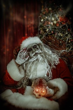 Zombi Noel Baba örümcek ağlarına dolanmış bir Noel süsüyle bir sandalyede oturuyor ve yanan gözlerle kafatasını tutuyor. Noel ve Cadılar Bayramı. 