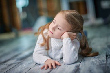 Beyaz kazaklı ve kotlu küçük sarışın bir kızın portresi. Tavan arasında düşünceli bir şekilde yatıyordu. Hayal kurarak yan tarafa bakıyordu. Mutlu çocukluk.