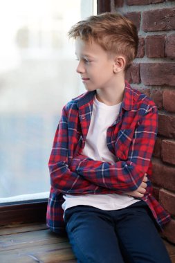 Ekose gömlekli ve kotlu şık, tasasız bir çocuk pencere eşiğine yaslanmış pencereden dışarı bakıp gülümsüyor. Çocuklar ve çocukluk. 