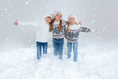 Kış aktiviteleri. Üç sevimli, neşeli çocuk şık örgü süveter ve şapkalarla karlı bir ortamda poz veriyor. Tam boy stüdyo resmi. Çocukların kış modası.. 